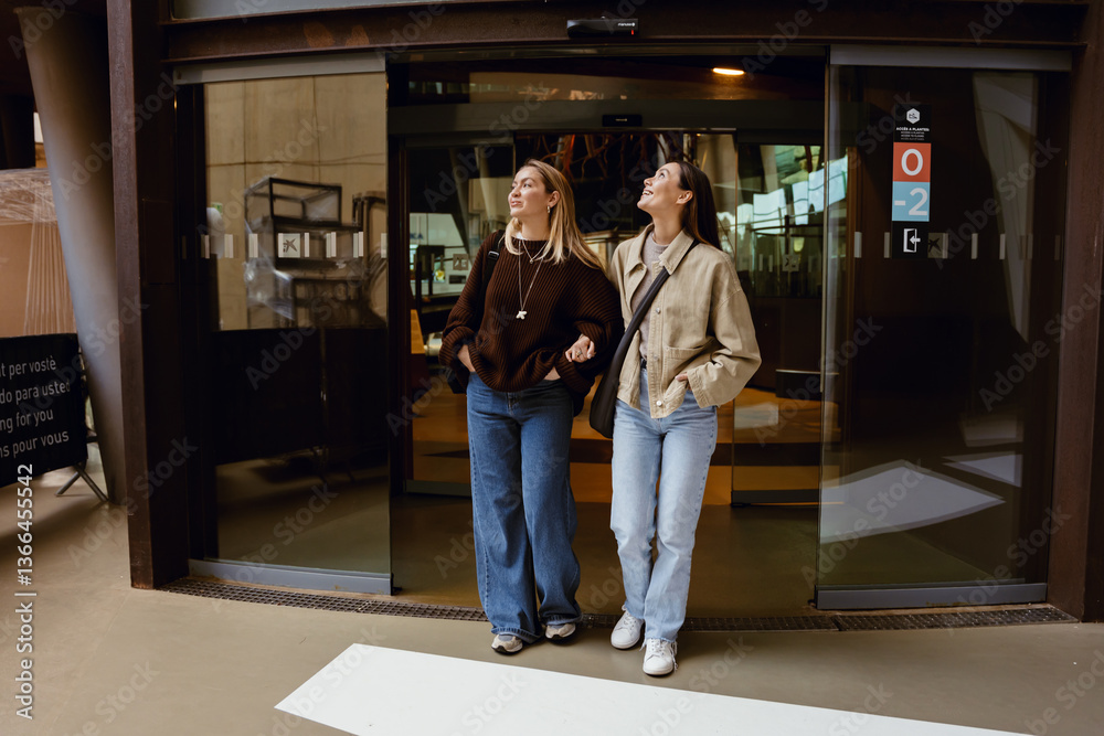 Fototapeta premium A woman walks and smiles while looking up and holding the arm of a friend walking next to her, during a trip