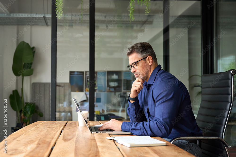 © insta_photos - Busy business man of middle age using laptop sitting at office desk. Mature older professional businessman executive at work. 50 years old manager or investor working on computer technology.
