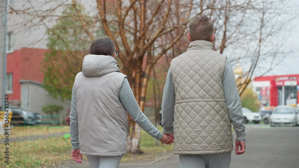 Back view of two couples walking hand in hand along quiet street in light-colored matching outfits, surrounded by trees and parked cars with soft natural lighting Back view of two couples walking hand in hand along quiet street in light-colored matching outfits, surrounded by trees and parked cars with soft natural lighting