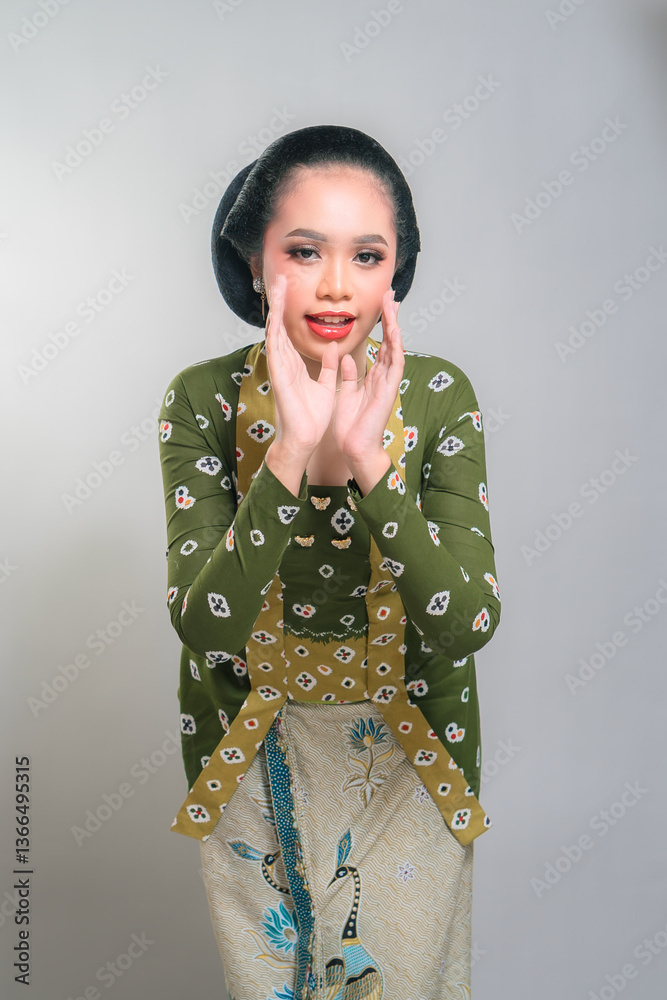 Indonesian woman in a green batik kebaya, smiling warmly with hands near face. Traditional elegance, cultural heritage, and joyful expression. Classic beauty, charming, and expressive. Indonesian woman in a green batik kebaya, smiling warmly with hands near face. Traditional elegance, cultural heritage, and joyful expression. Classic beauty, charming, and expressive.