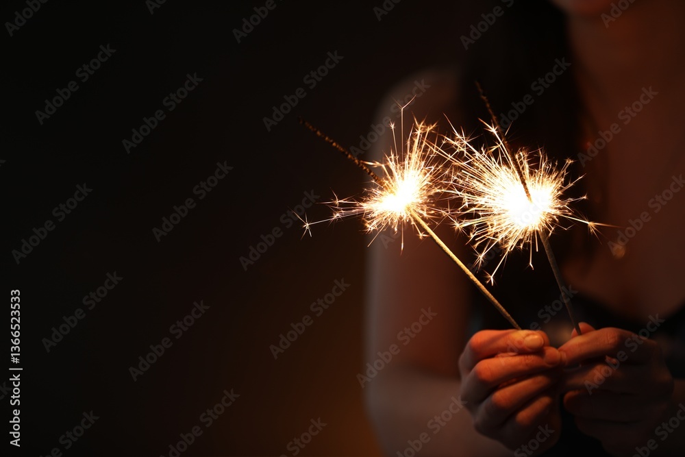 Woman with bright burning sparklers on dark background, closeup. Space for text