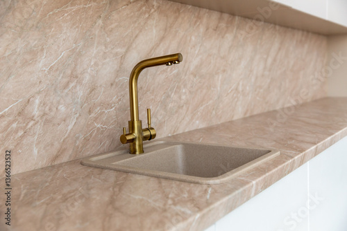 A golden faucet in a modern kitchen with a marble beige facade.