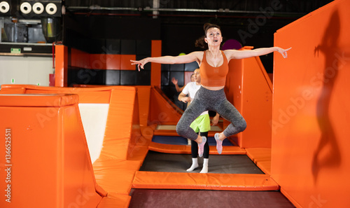 Capturing moment of elation, cheerful woman soaring while jumping at modern brightly colored trampoline park..