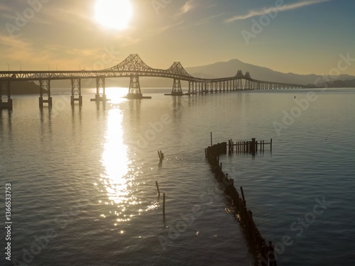 The  Richmond-San Rafael Bridge spans the San Pablo Bay in Richmond, California, USA, The photo captures the bridge at sunset, with sunlight reflecting on the water.
