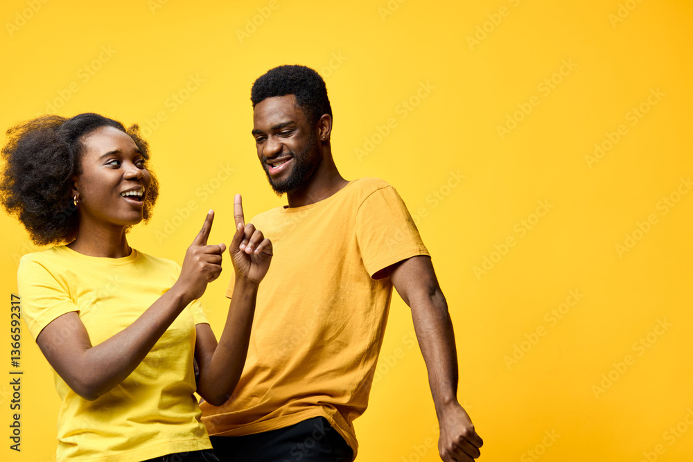 Obraz premium Happy African couple having fun and dancing against a bright yellow background, wearing casual yellow and black clothes, expressing joy and connection