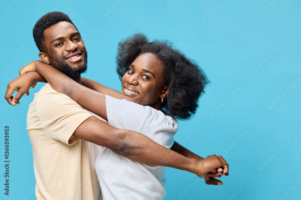 Obraz premium Happy young couple embracing against a vibrant blue background, showcasing joy and love in casual clothing, perfect for celebrating relationships and connection