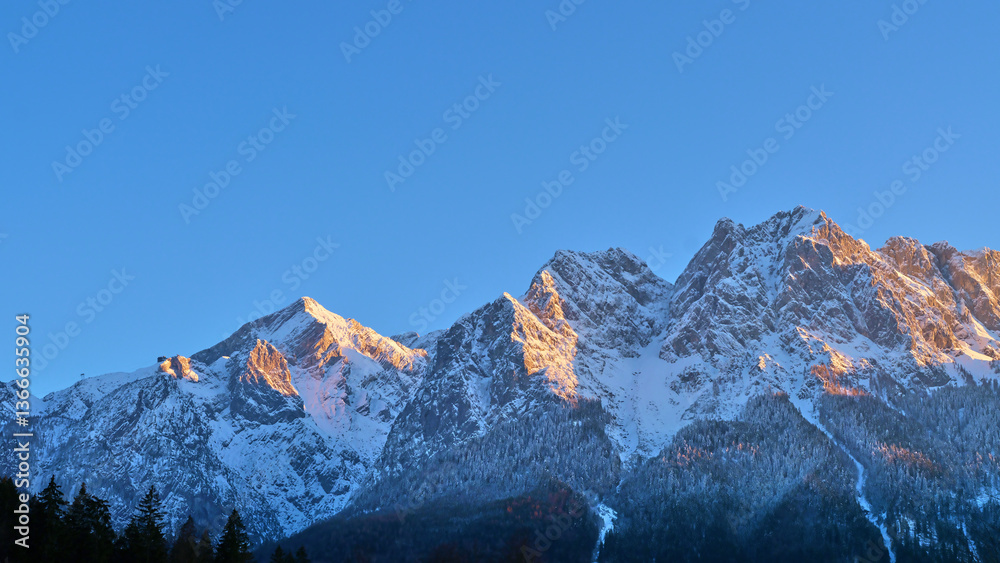 Snow-covered mountain peaks illuminated by morning light in a clear blue sky Snow-covered mountain peaks illuminated by morning light in a clear blue sky