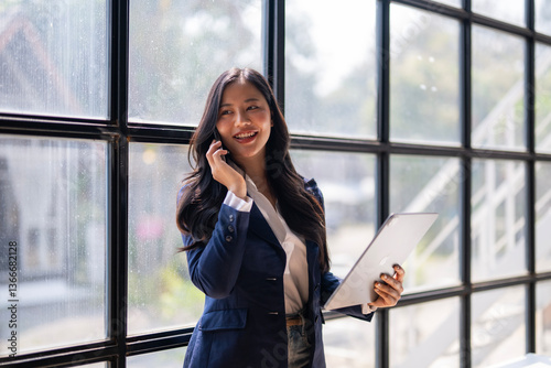 A woman in a business suit is talking on her cell phone while holding a tablet