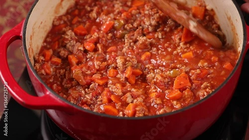 Cooking beef chili, simmering in a pot on a stove, stirring with a wooden spoon