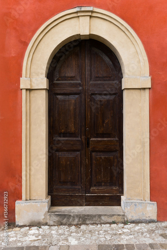 Historic wooden doorway with stone arch frame in vibrant red wall.