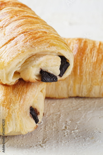 A single pain au chocolate pastry placed on a white textured surface, showcasing its golden, flaky layers and rich chocolate filling.