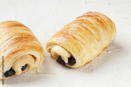 A single pain au chocolate pastry placed on a white textured surface, showcasing its golden, flaky layers and rich chocolate filling.