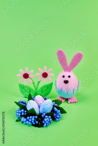 funny toy easter pink bunny preparing for the holiday with colorful eggs and flowers on a green background