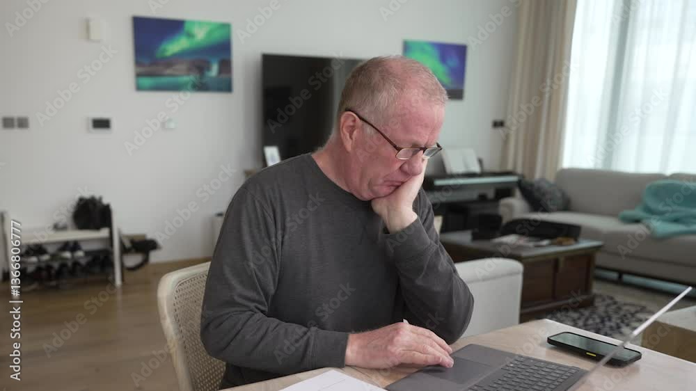 Older man working on a laptop computer at home looking stressed Older man working on a laptop computer at home looking stressed