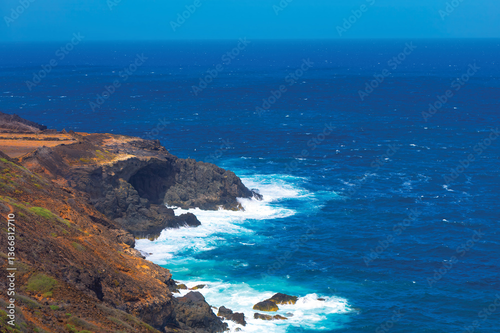 Dramatic coastal cliffs meet the restless ocean, waves crashing against the dark volcanic rock. Landscape of Pacific Ocean shore