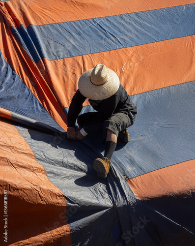 Eye level with a worker wearing a straw hat installing an orange and blue  fumigation tent on a house