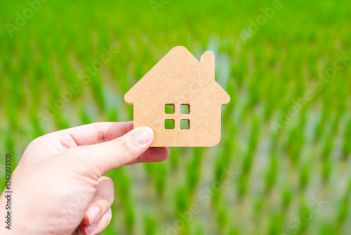 Conservationists hold up a house symbol against a background of growing rice, the concept of sustainable coexistence with nature and a self-sufficient economy.