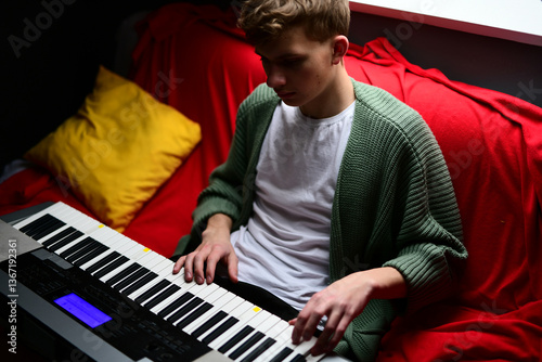 Young man plays synthesizer, musician guy composes track on keyboard sitting on sofa at home photo