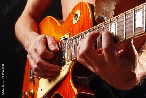 Hands of musician playing the orange guitar on dark stage.