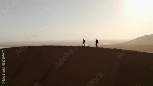 Two girls with big backpacks walking on top of a dune with a river valley in the background in the Altyn Emel national park, Kazakhstan