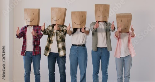 People with paper bags on their heads, each decorated with happy face, give enthusiastic thumbs up. Group of anonymous people stand in row and give positive feedback about customer satisfaction.