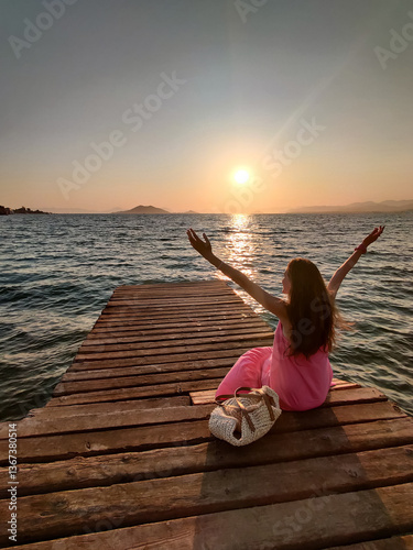 a beautiful girl sits on a sea pier at sunset