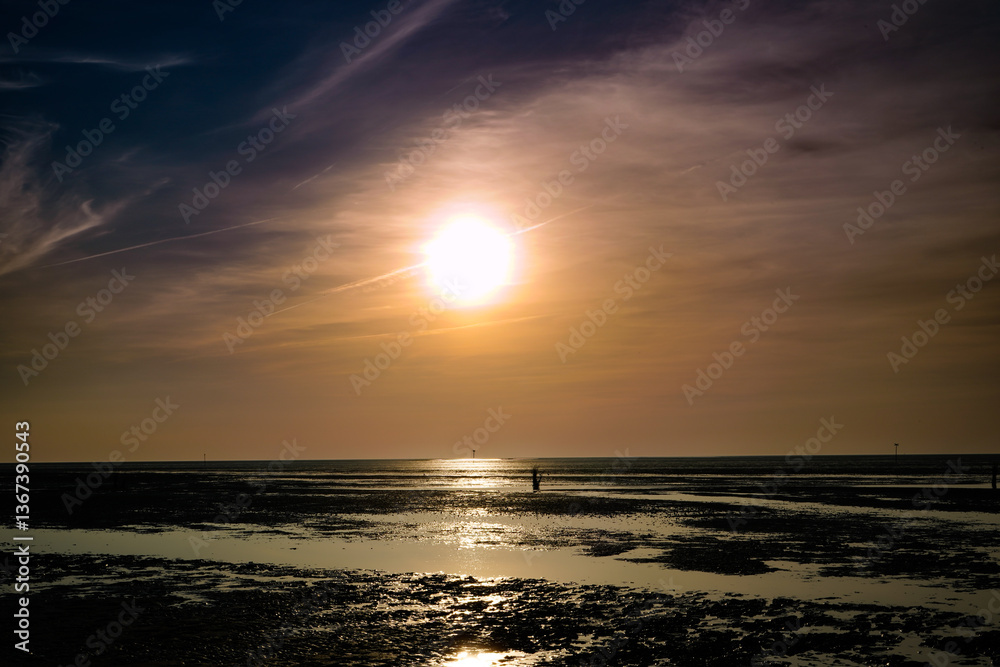 Obraz premium Ein sonniger Frühlingstag geht zu Ende und die untergehende Sonne steht schon tief über dem Wattenmeer bei Sahlenburg, Deutschland.