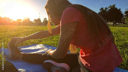 Obraz na płótnie Young woman exercising on a sports yoga mat on the grass in a park during summertime sunset time. w salonie