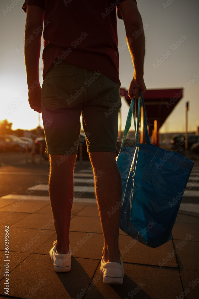 Man with shopping bag on a market parking lot in sunset time.