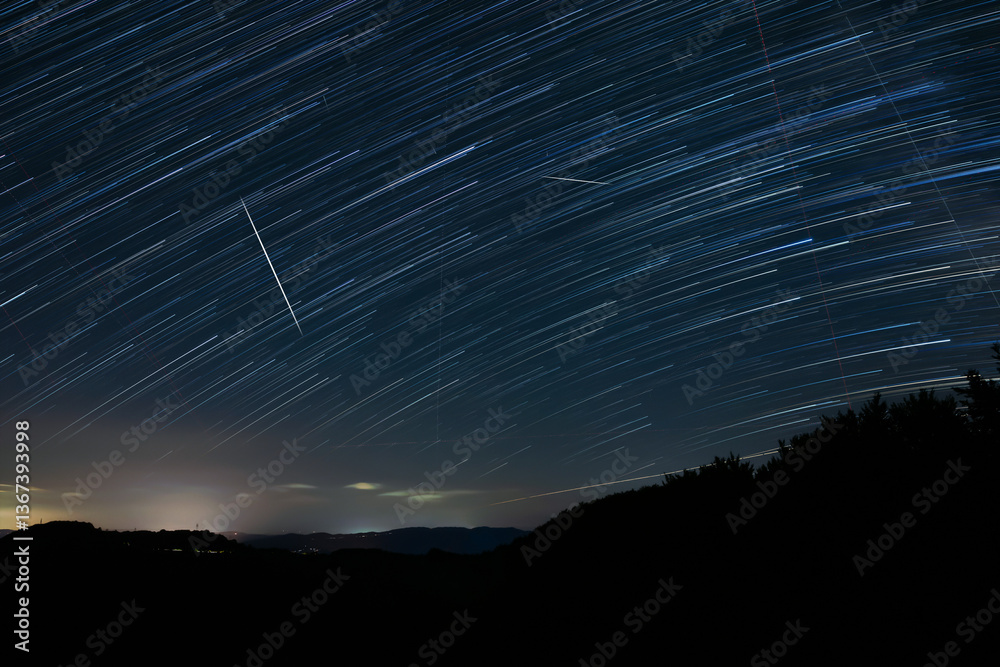 Star trails of a Milky Way with meteor, shooting stars and landscape silhouettes.