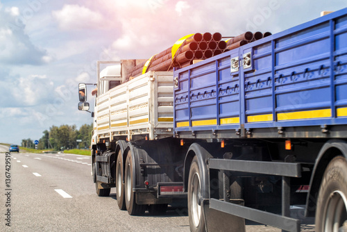 Transporting metal pipes on a semi-trailer truck along a highway in summer, industry. Transportation of metal products. Copy space for text, cloudy sky