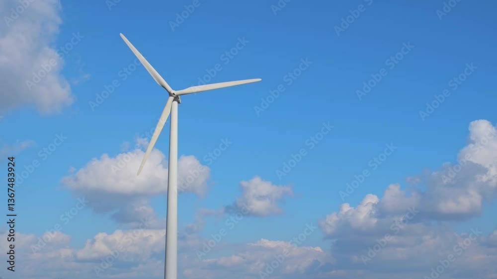A wind generator rotates against a cloudy blue sky and produces electricity. Green energy concept, which is generated from natural resources such as wind, sun, water. A wind generator rotates against a cloudy blue sky and produces electricity. Green energy concept, which is generated from natural resources such as wind, sun, water.
