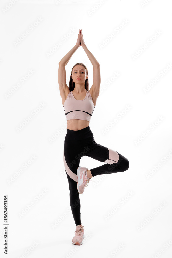 Woman practicing yoga with tree pose in activewear against a plain background during a calm indoor session Woman practicing yoga with tree pose in activewear against a plain background during a calm indoor session