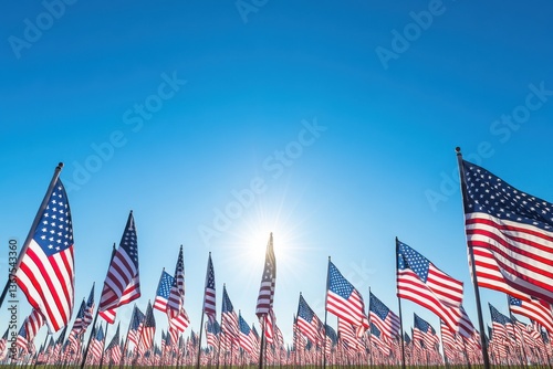 A field of american flags waving proudly beneath a clear blue sky with the sun shining brightly above them all