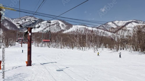 Skiers on gentle slope, trees, mountain. POV from chairlift. Hakuba