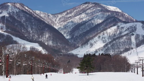 Skier and snowboarders on wide slope with mountain backdrop. Hakuba
