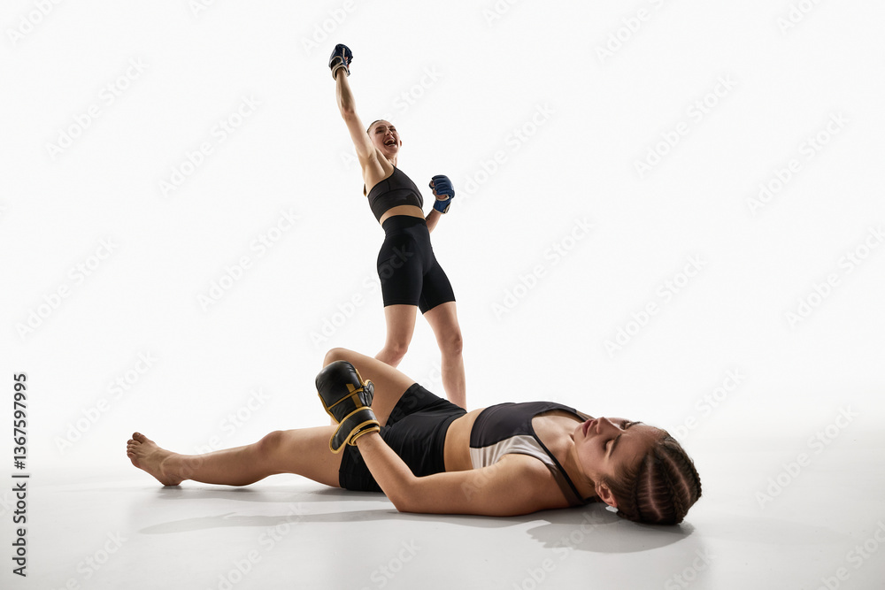 Obraz premium Victorious female fighter in sportswear and gloves celebrating win standing over defeated opponent on white background. Concept of MMA, Thai boxing, sport, power, fight, athleticism, action.