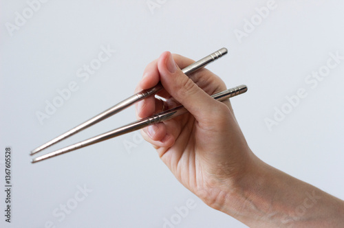 human hand holding modern reusable eco-friendly korean metal chopsticks isolated on white background, cutlery concept, environmentally-friendly cutlery 