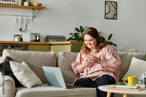 Joyful young woman with Down syndrome enjoying a cozy moment at home while using her laptop