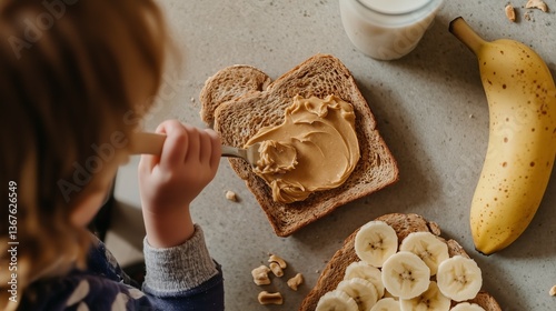 A child spreads peanut butter on bread next to sliced bananas and a glass of milk for a wholesome snack.