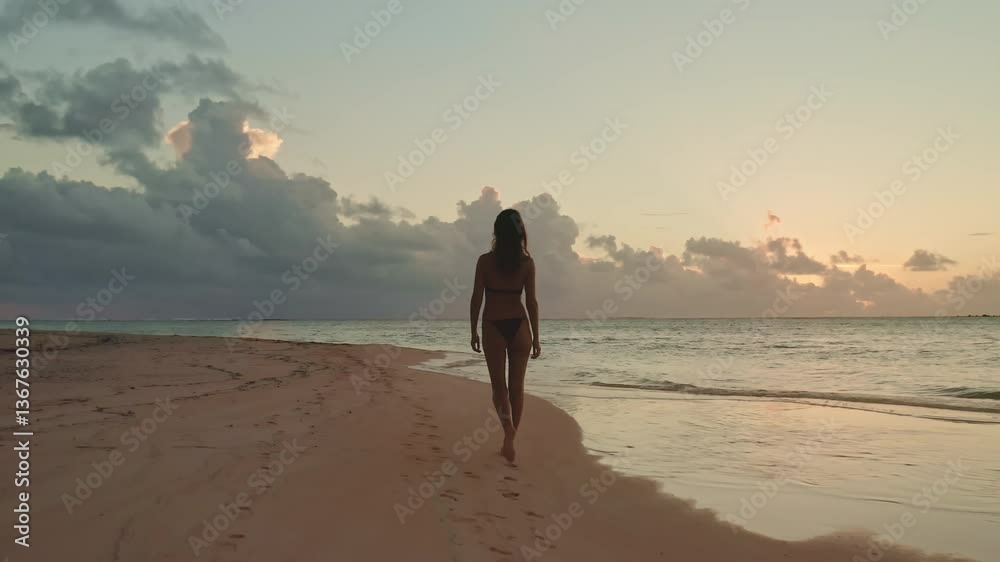 Young woman is enjoying a peaceful walk on the beach as the sun sets over the indian ocean, casting a warm glow on the water and sand
