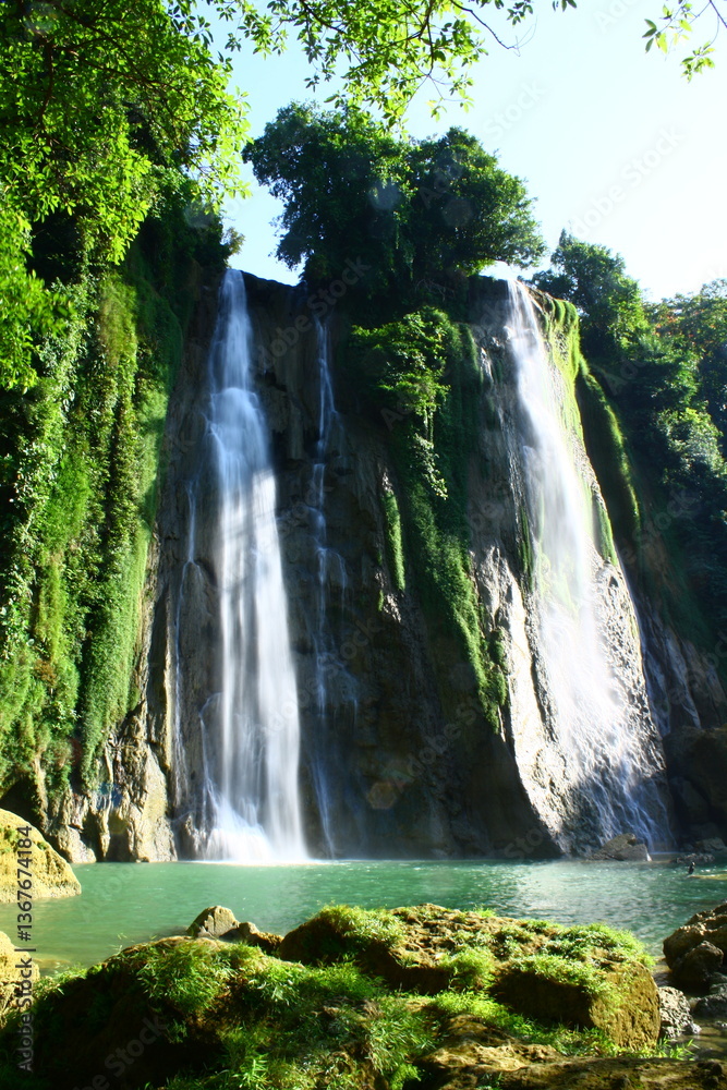 Naklejka premium A breathtaking photograph captures a stunning waterfall cascading down rocky cliffs, surrounded by lush greenery, with mist rising beautifully into the fresh, crisp air.
