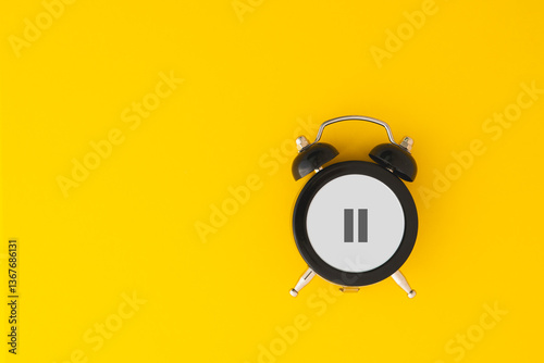 Black alarm clock with pause sign on yellow background including copy space, for take a break, overworked concept, hormone replacement therapy