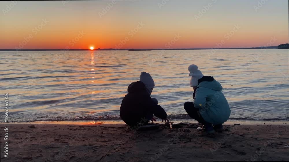 Children playing near water in evening. Kids digging hole on shore at sunset. Keep children safe around water.