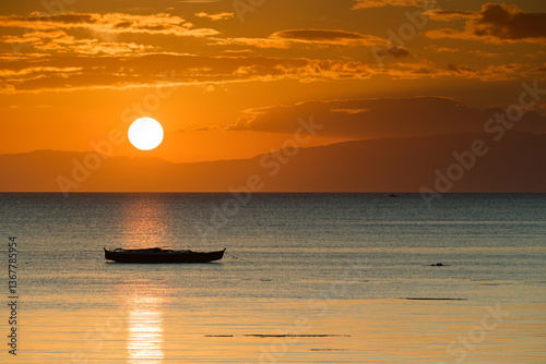 Serene Sunset Over Ocean with Silhoutted Boat and Warm Tones