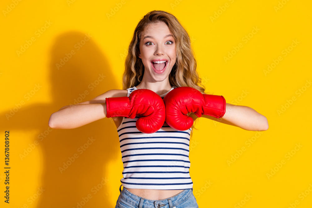 Fototapeta premium Cheerful Young Woman in Striped Top With Boxing Gloves Posing Against a Yellow Background With Vibrant Energy