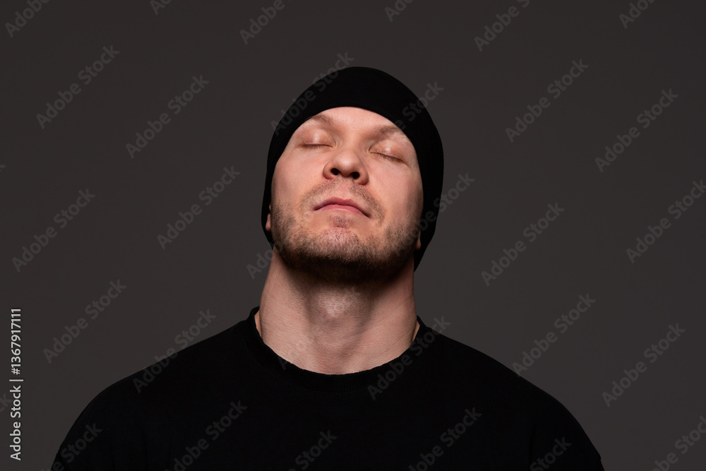 Fototapeta premium Man in black beanie and sweatshirt with closed eyes, calm expression