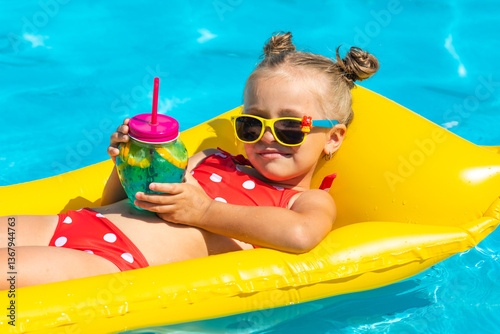 Cute child, little girl lying on yellow inflatable mattress in swimming pool in sunglasses, drinks a mojito cocktail. Summer vacation concept.