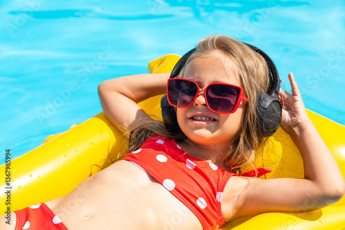 Obraz na płótnie Happy little girl lying on inflatable mattress in swimming pool and listening to music via headphones. Close up portrait of child in swimsuit in wireless headphones. Tropical summer vacation concept w salonie