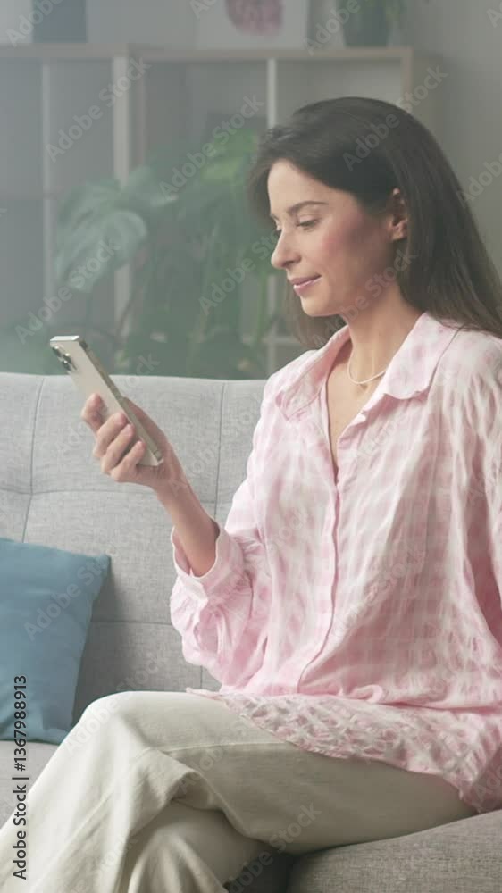 Woman relaxes on a modern couch, reading messages on her smartphone in a cozy living room with colorful cushions and plants. 4K video, slow motion, 50 fps Woman relaxes on a modern couch, reading messages on her smartphone in a cozy living room with colorful cushions and plants. 4K video, slow motion, 50 fps